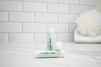 Two lip balms labeled 'Vanilla Mint' on a bathroom counter with a tiled wall background.