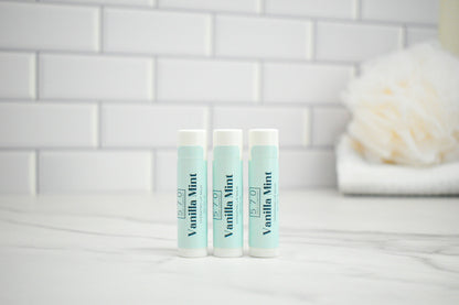 Three lip balm tubes labeled 'Vanilla Mint' on a bathroom counter with a tiled wall background.