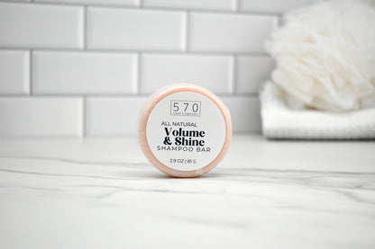 Shampoo bar container labeled '570 Volume & Shine Shampoo Bar' on a bathroom counter.