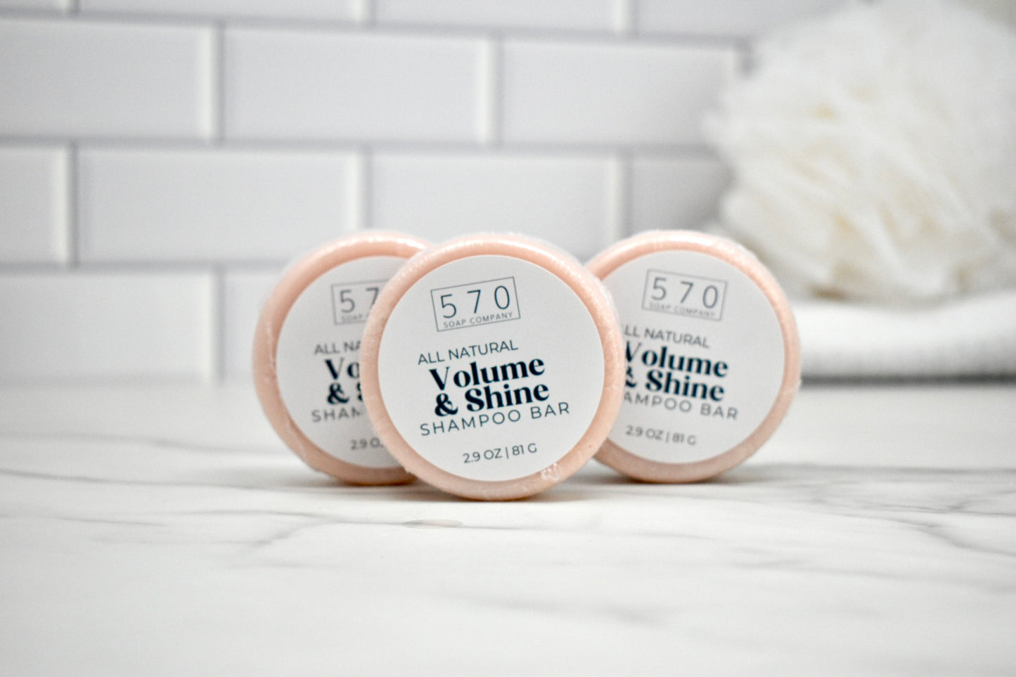Three shampoo bars labeled '570 Volume & Shine' on a white surface with a tiled wall background.