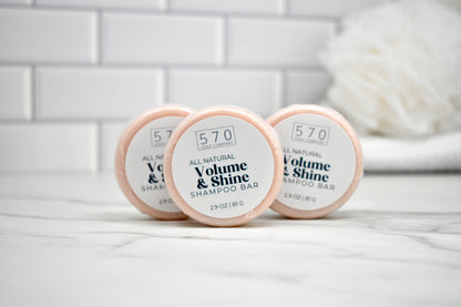 Three shampoo bars labeled '570 Volume & Shine' on a white surface with a tiled wall background.