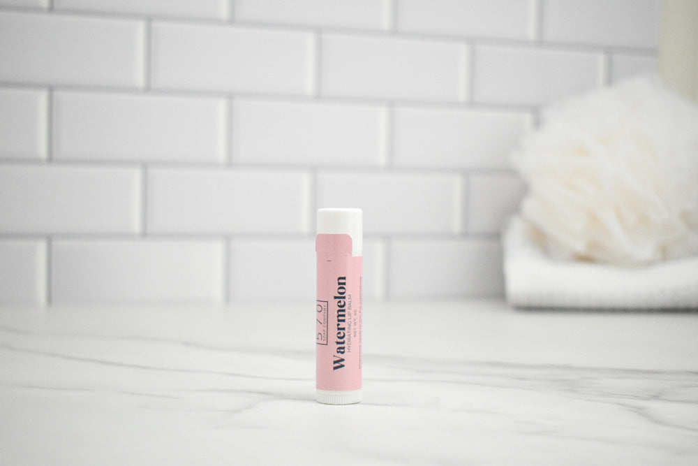 Pink lip balm with 'Watermelon' flavor on a white surface against a tiled wall background