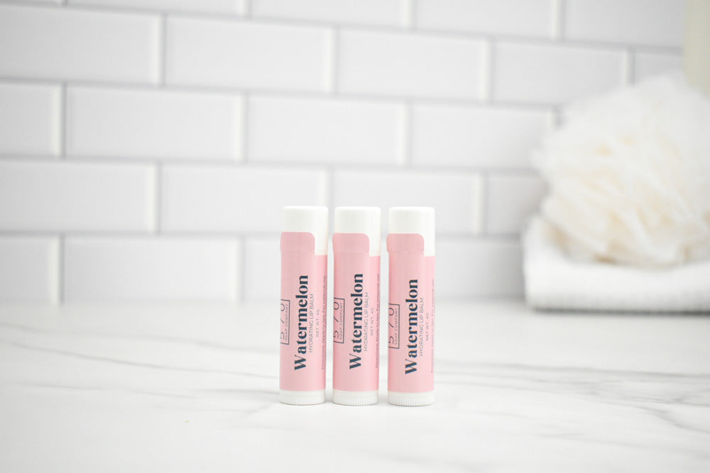 Three lip balm tubes labeled 'Watermelon' on a white surface with a tiled wall background.