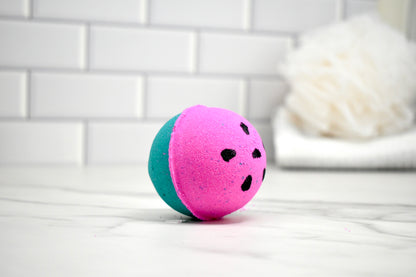 Two-toned pink and teal bath bomb on a white surface with a blurred background