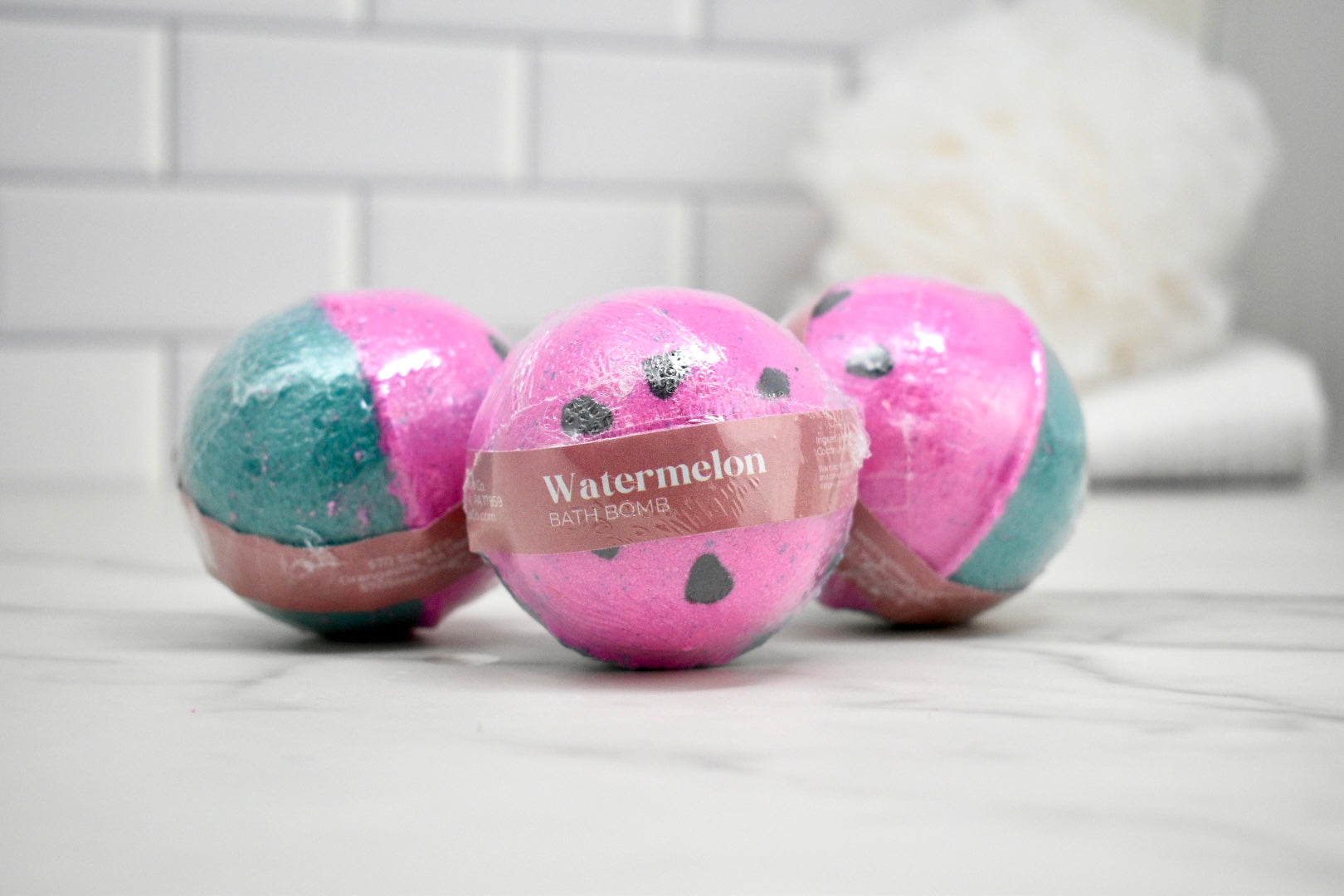 Three bath bombs, two pink and one multicolored, on a tiled surface.