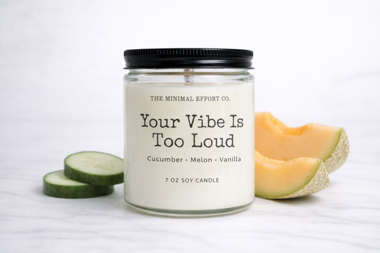 Candle labeled 'Your Vibe Is Too Loud' with cantaloupe slices on a white background