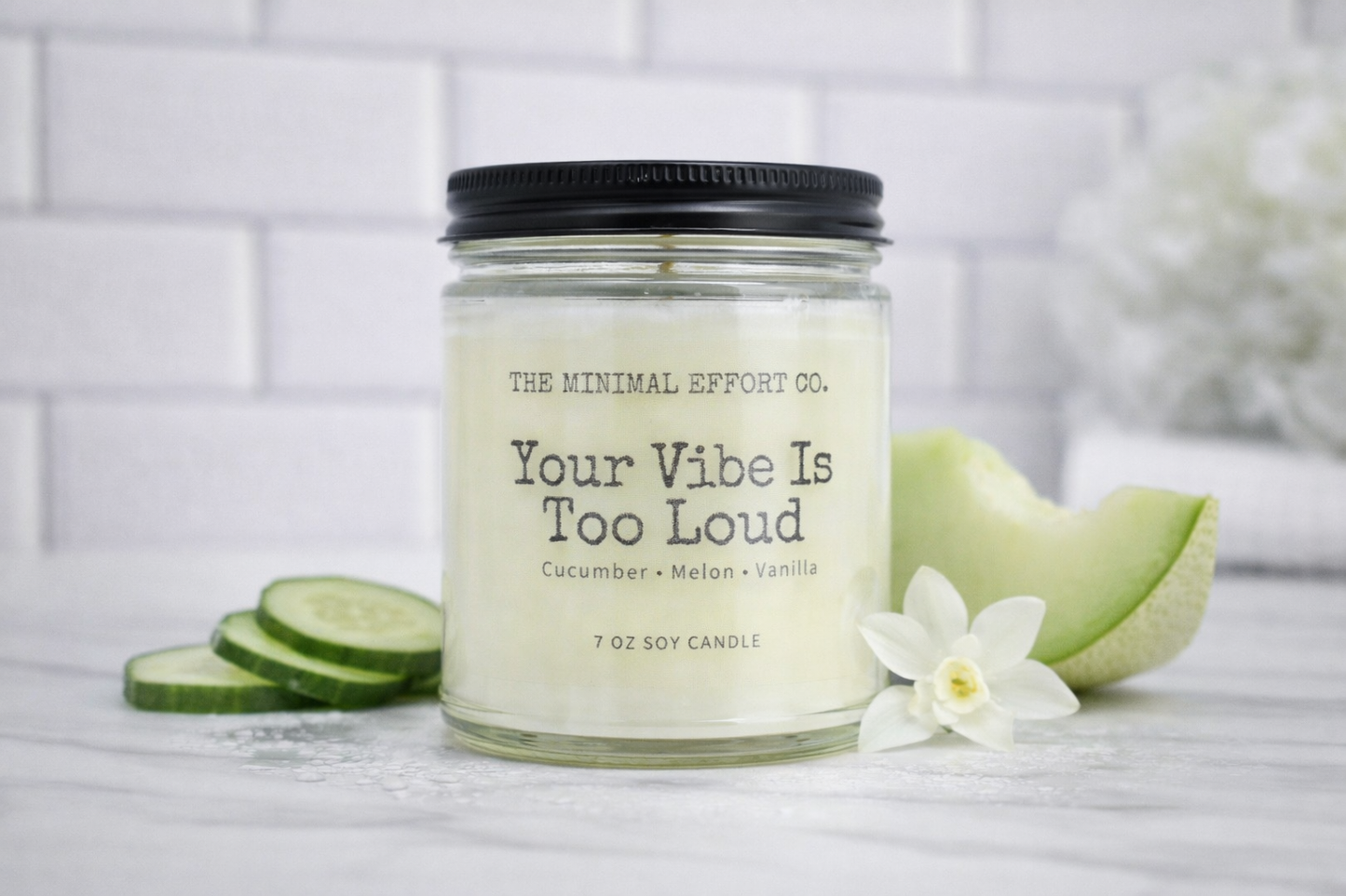 Candle jar labeled 'Your Vibe Is Too Loud' with cucumber slices and a flower on a white background